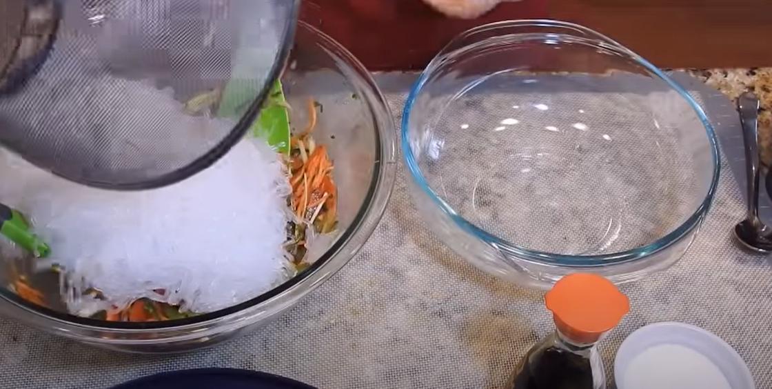 Фунчозу высыпают в салатницу к овощам из дуршлага, рядом стоит стеклянная тарелка