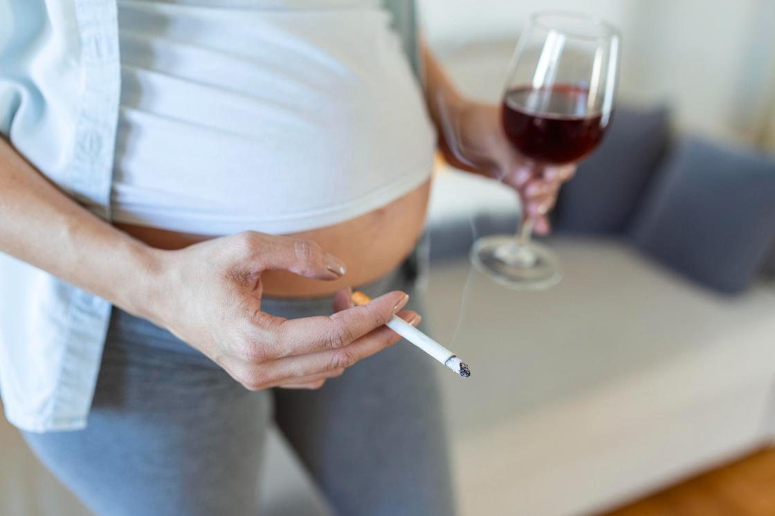Беременная женщина держит бокал с вином и сигарету