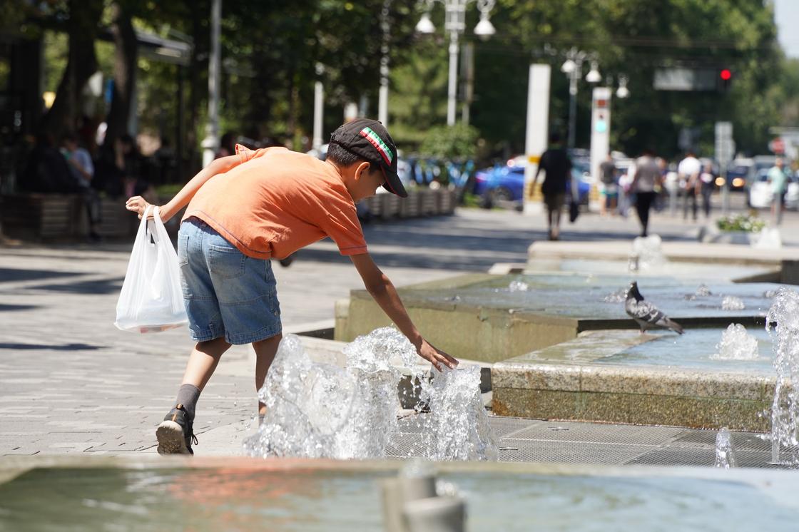 Мальчиу трогает воду у фонтана в Алматы