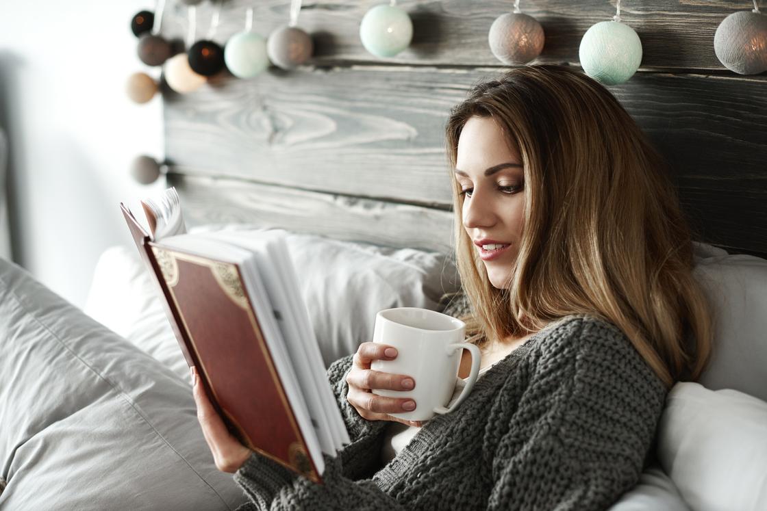 Девушка пьет чай и читает книгу в постели