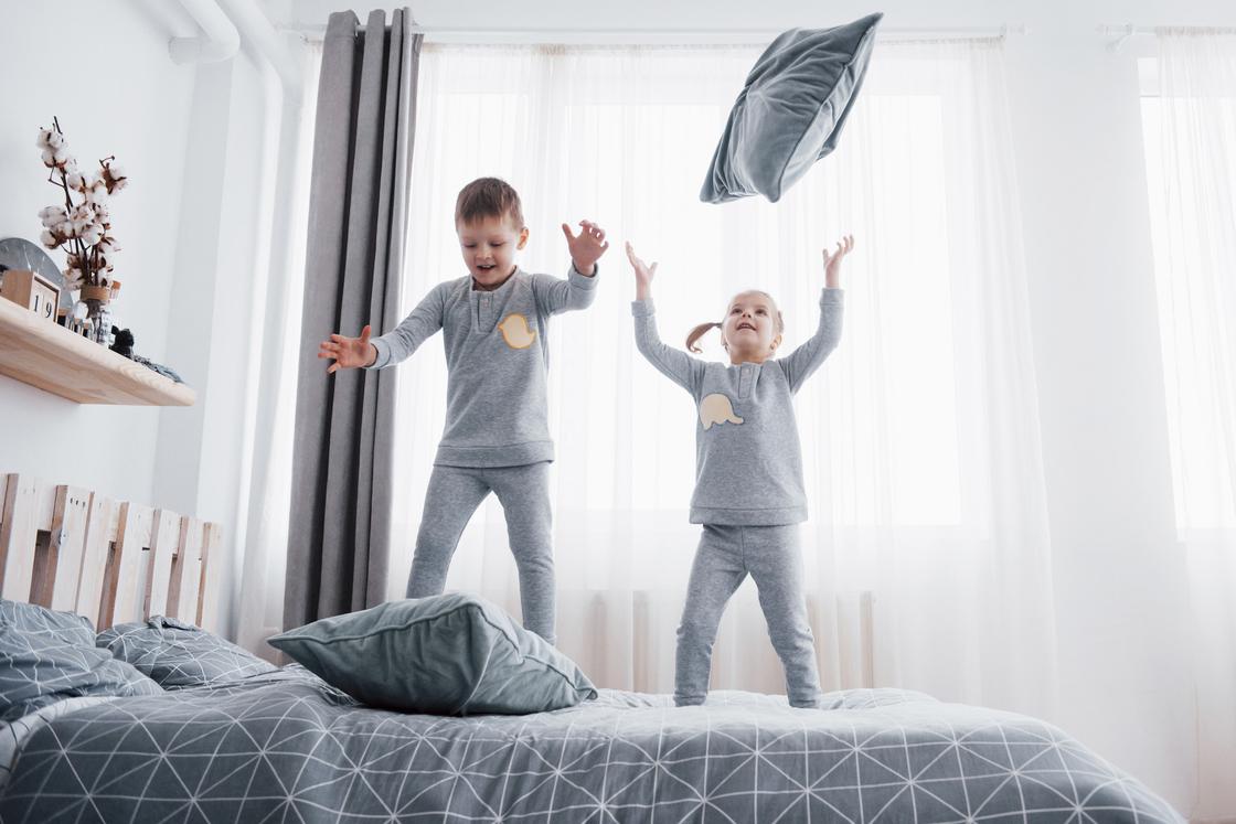 Дети прыгают на кровати и бросают подушки