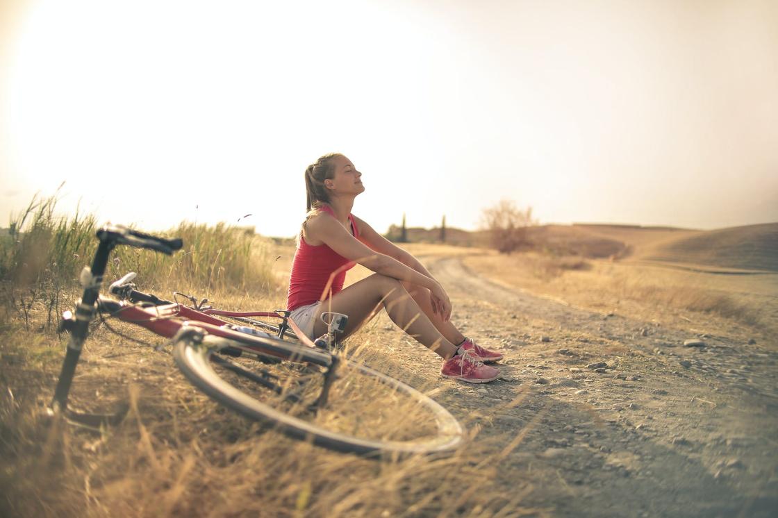 Девушка сидит в поле рядом с велосипедом