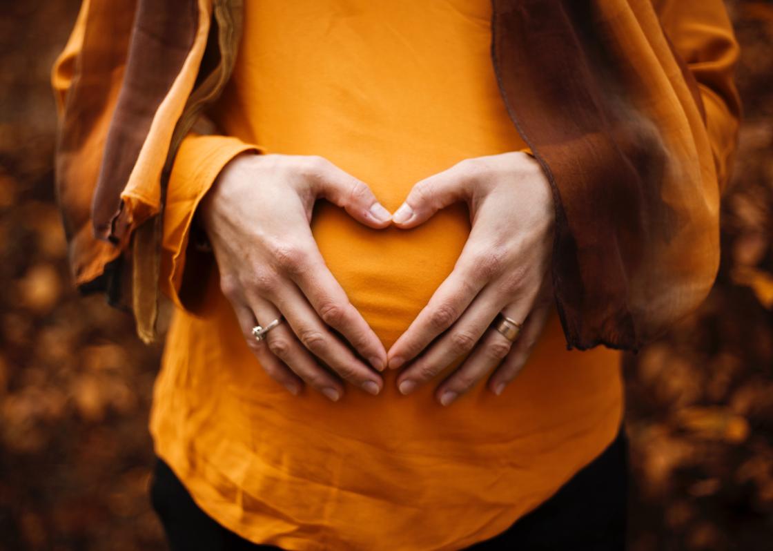 Беременная девушка держит руки на животе