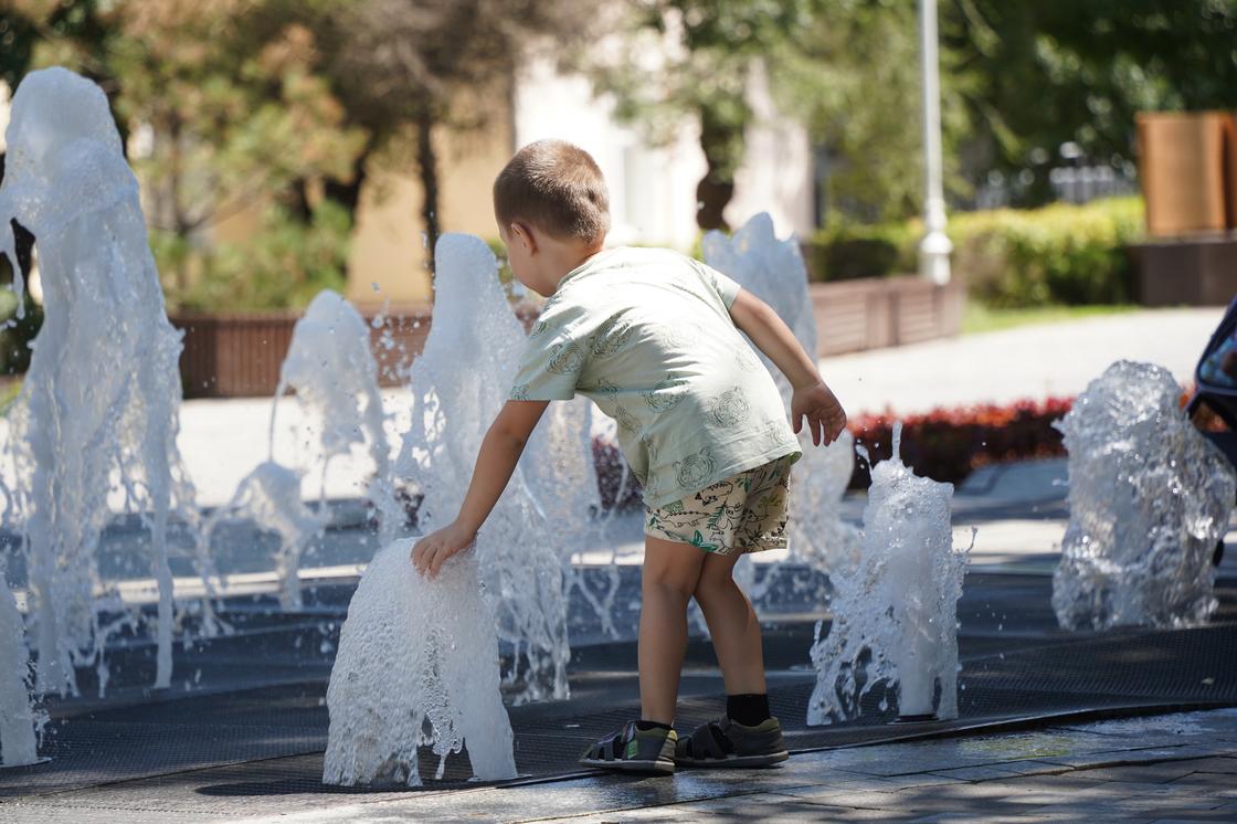 Мальчик трогает руками воду из фонтана