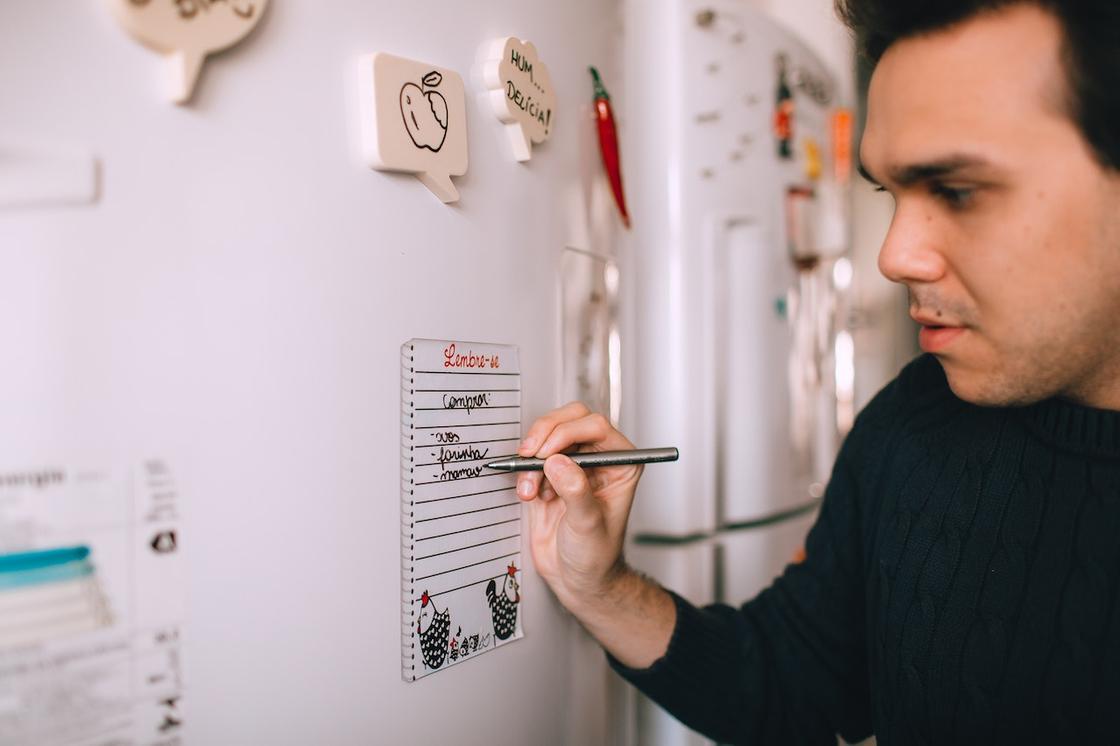 Мужчина пишет напоминание на холодильнике