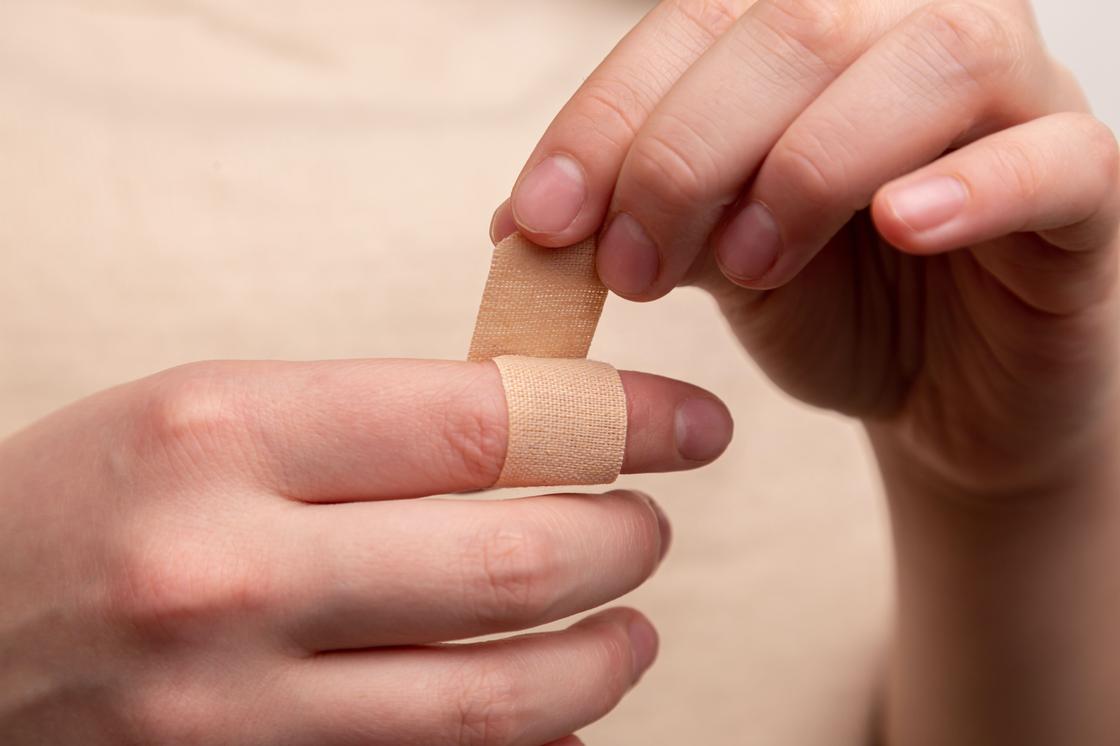 Девушка заклеивает рану на пальце пластырем