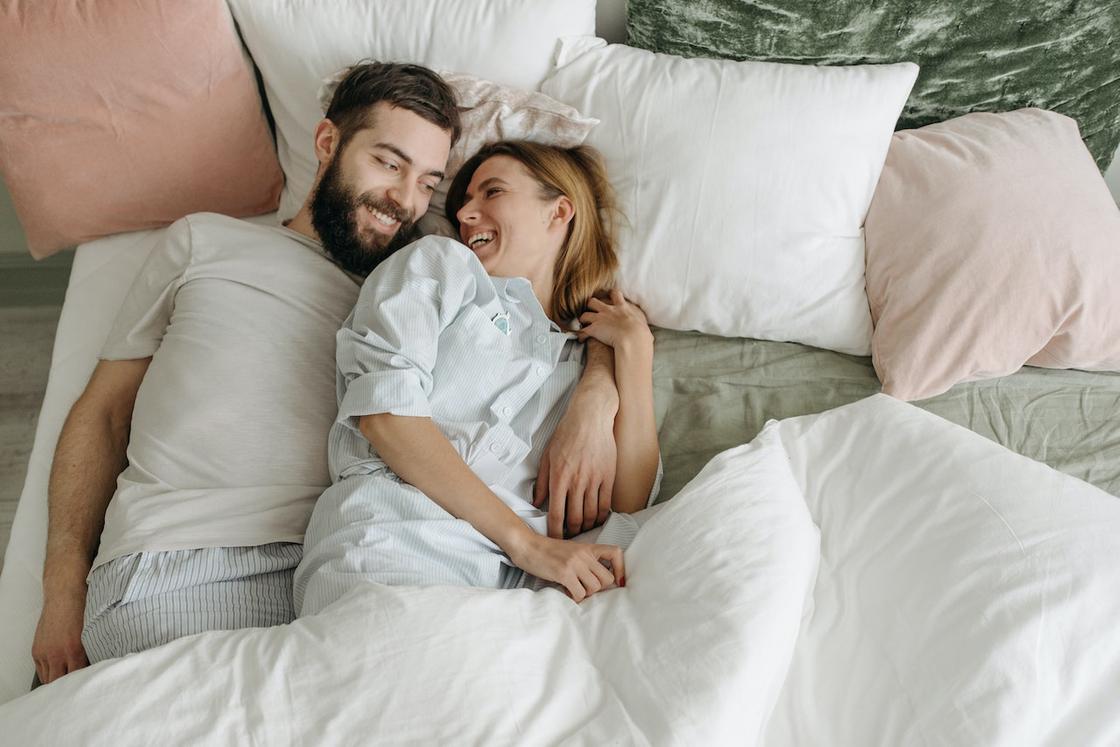 Мужчина и женщина улыбаются друг другу, лежа в постели
