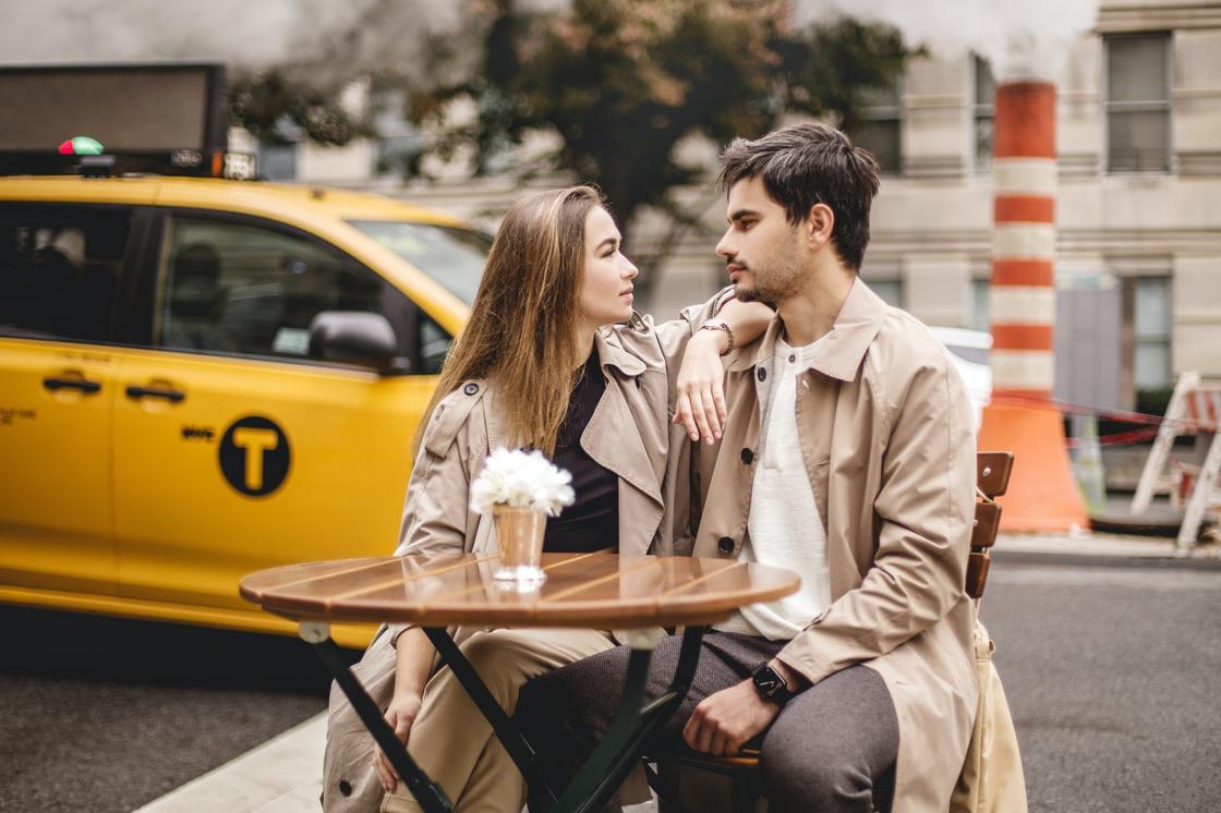 Парень и девушка сидят за столиком уличного кафе на фоне проезжающего такси