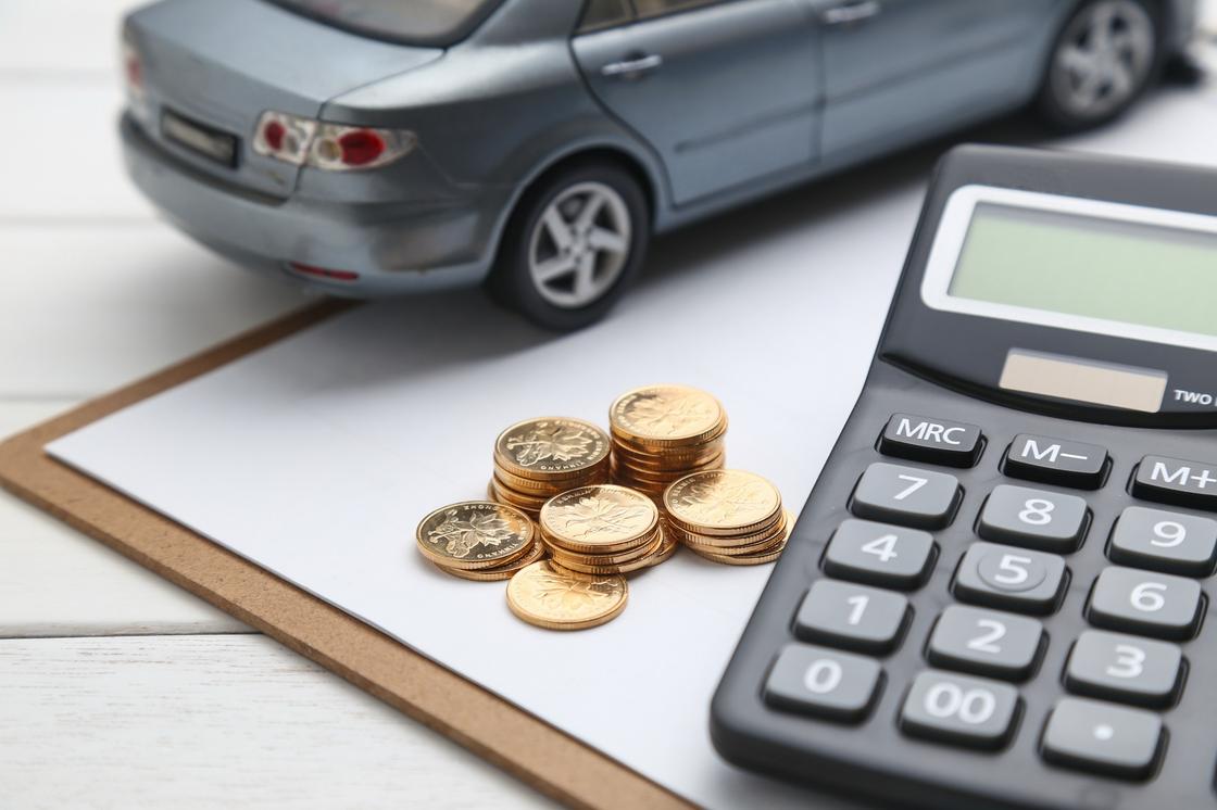 На столе стоить моделька авто, лежат стопки монет и кулькулятор