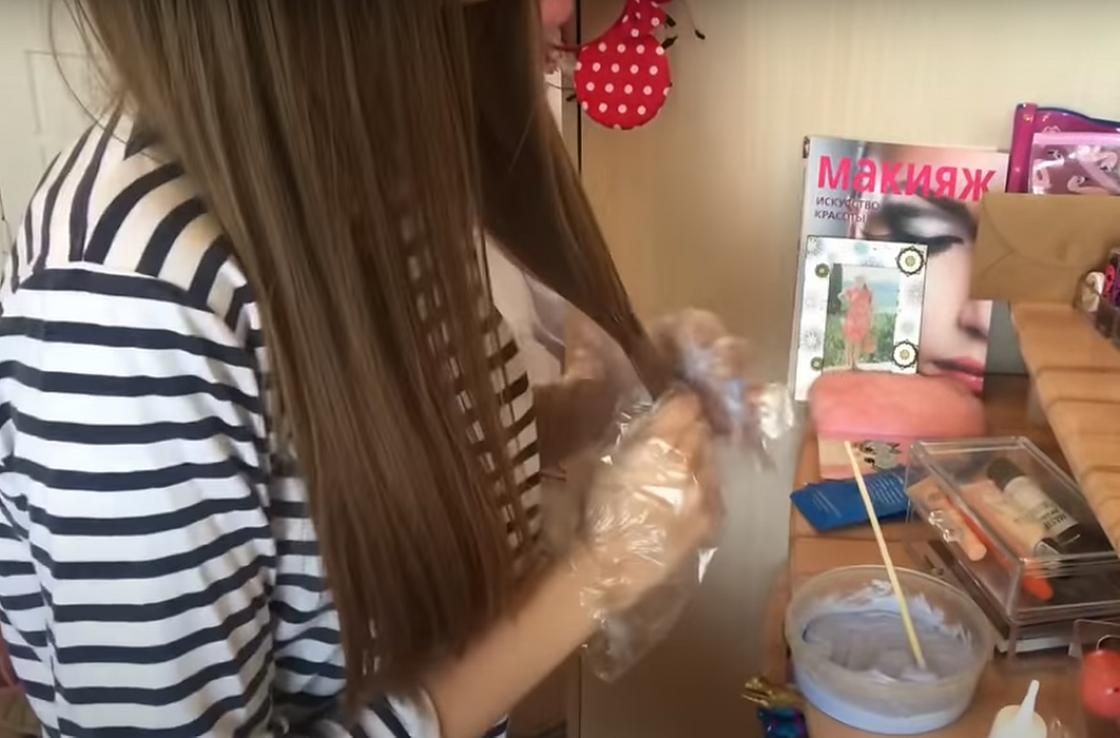 Девушка прокрашивает кончики волос осветлителем