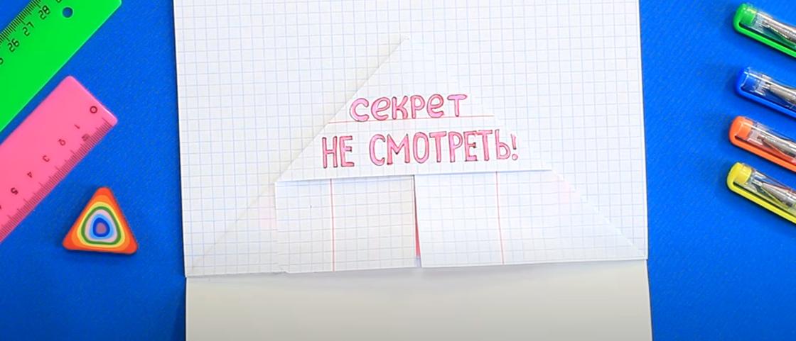 В тетради в клеточку сложен треугольный конверт из листа с надписью