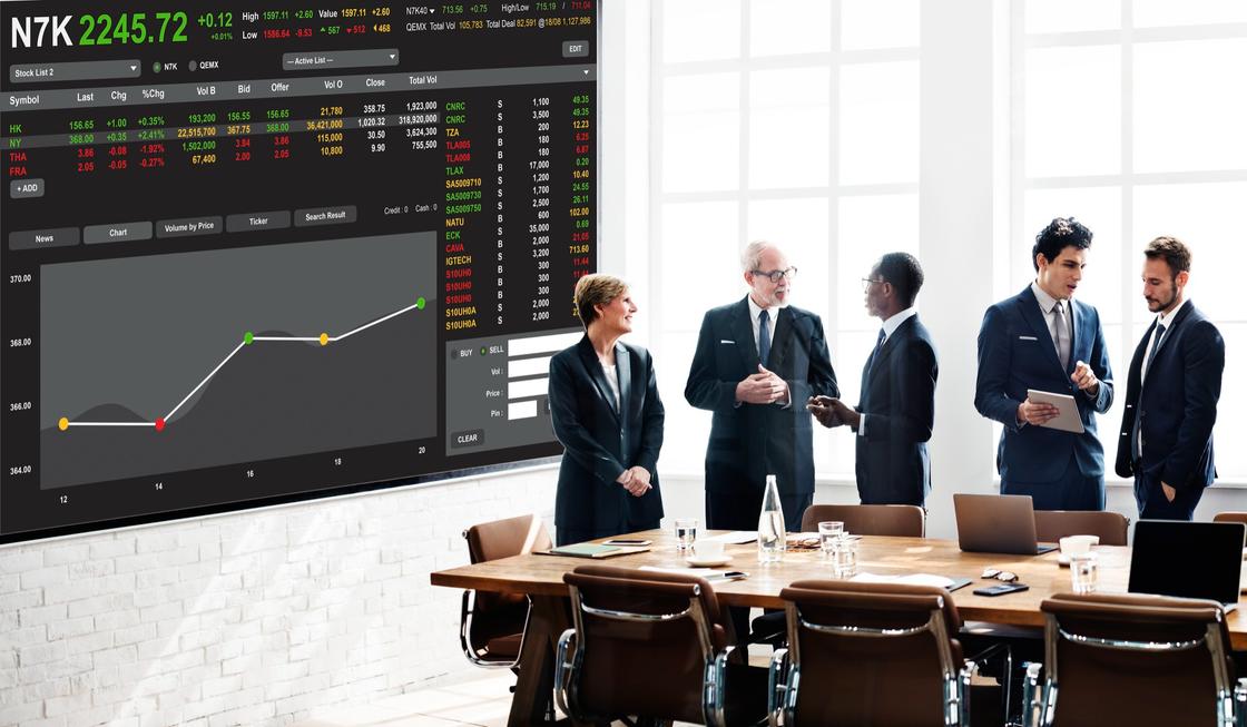 Люди в деловых костюмах стоят на фоне экрана фондовой биржи