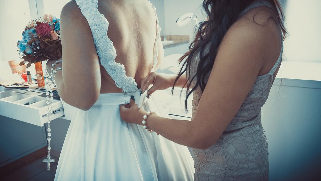 Девушка помогает невесте надеть платье