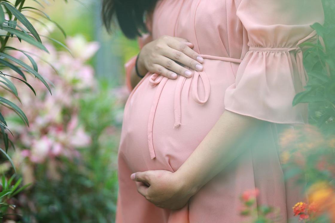 Беременная женщина в розовом платье на природе