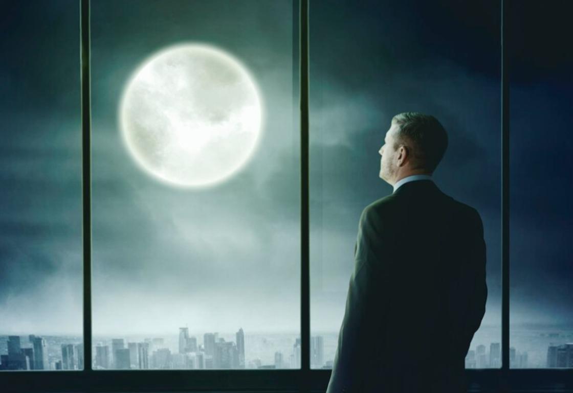 Мужчина стоит перед окном, глядя на Луну