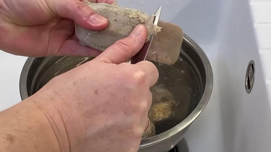 Над миской с водой очищают сваренный свиной язык от оболочки