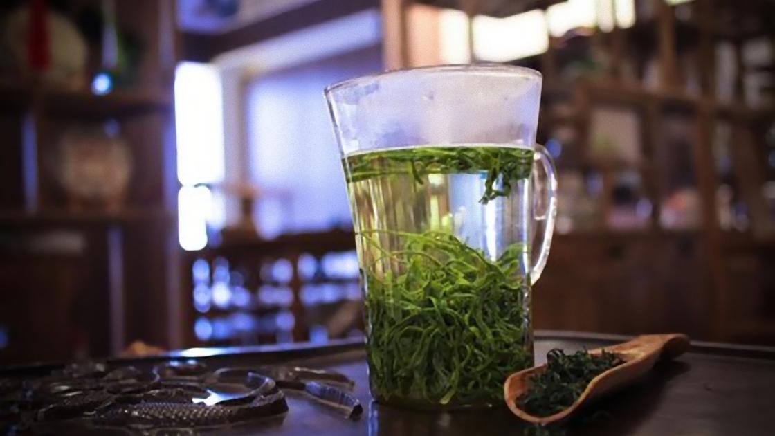 Зеленый чай в прозрачной чашке, сухая заварка в деревянном ковшике