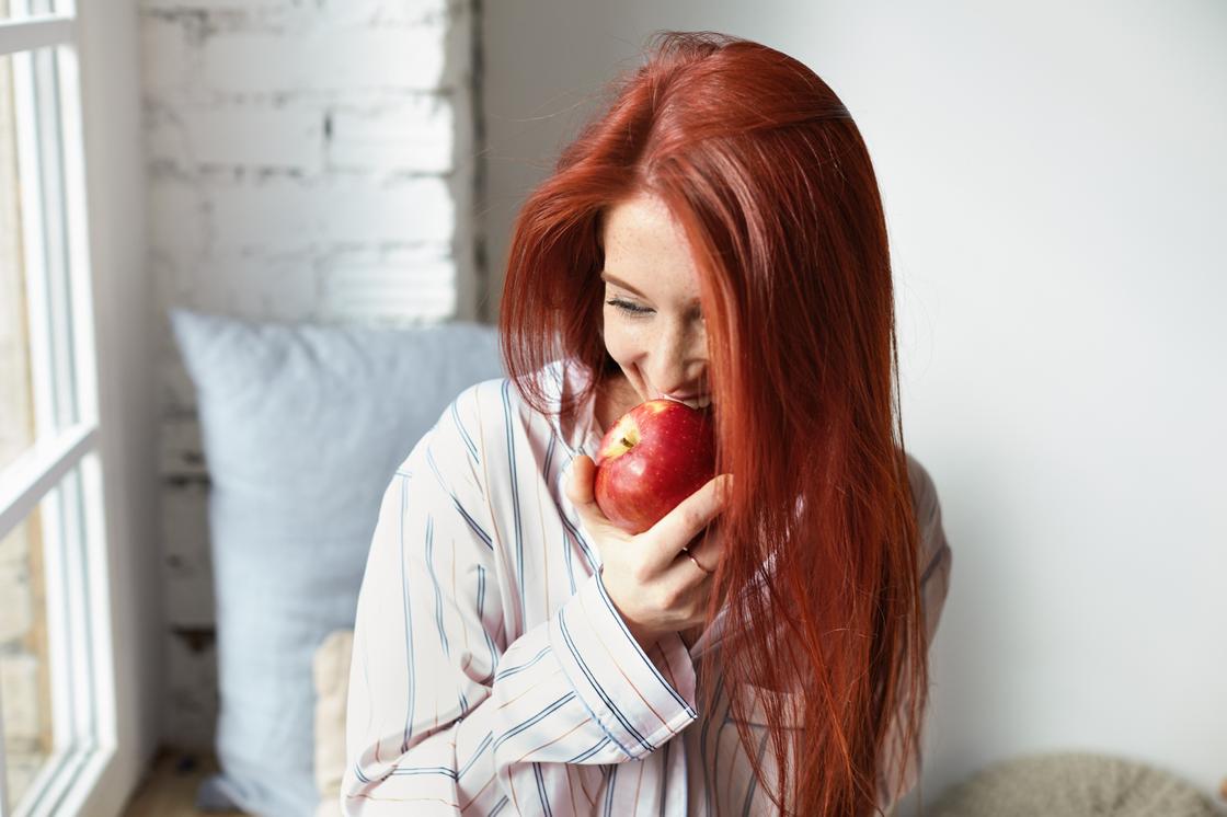 Девушка с окрашенными в красный цвет волосами кусает яблоко