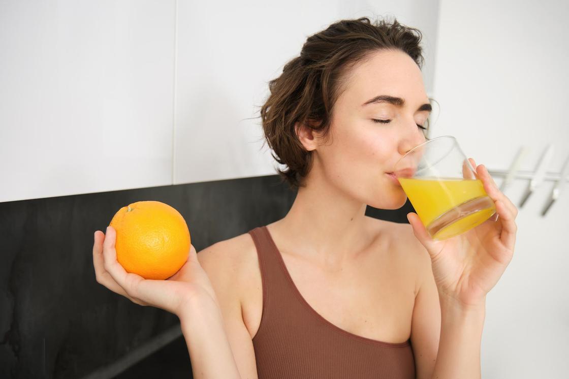 Девушка пьет апельсиновый сок из стакана