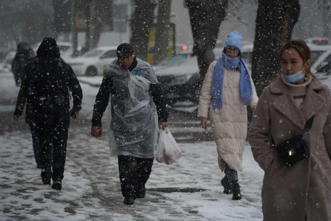Люди идут по улице во время снегопада в Алматы