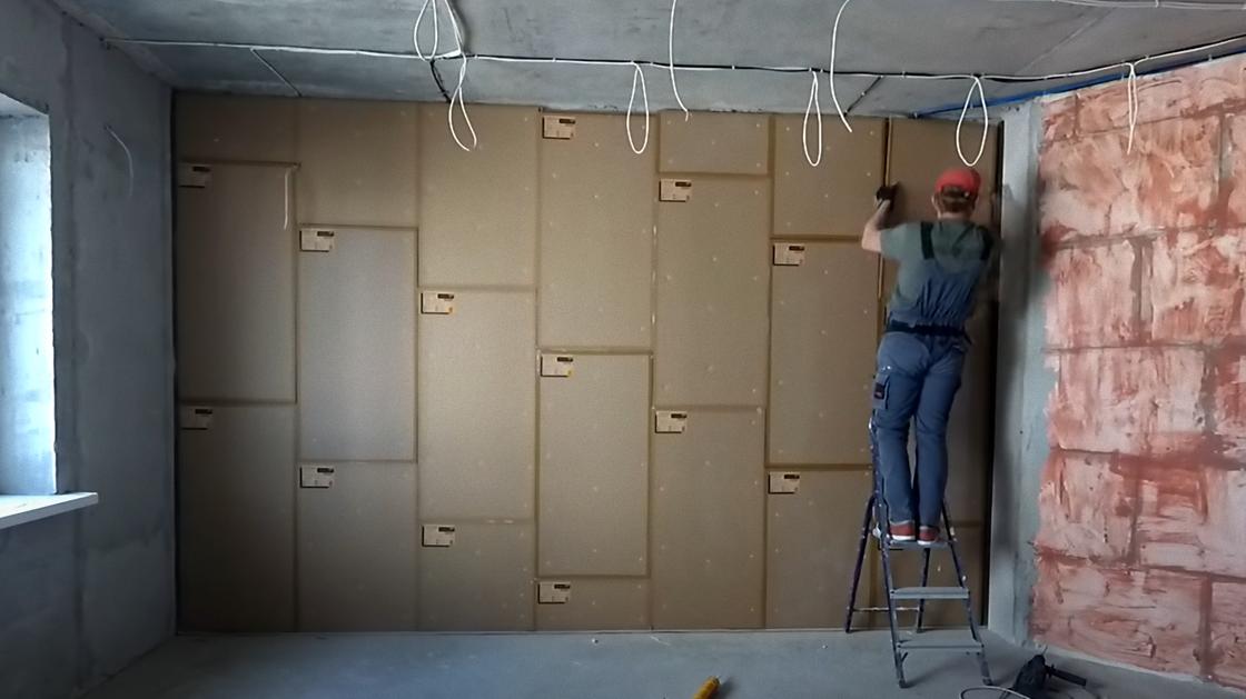 Строитель на лесенке заканчивает прикреплять шумопоглощающие панели на стене