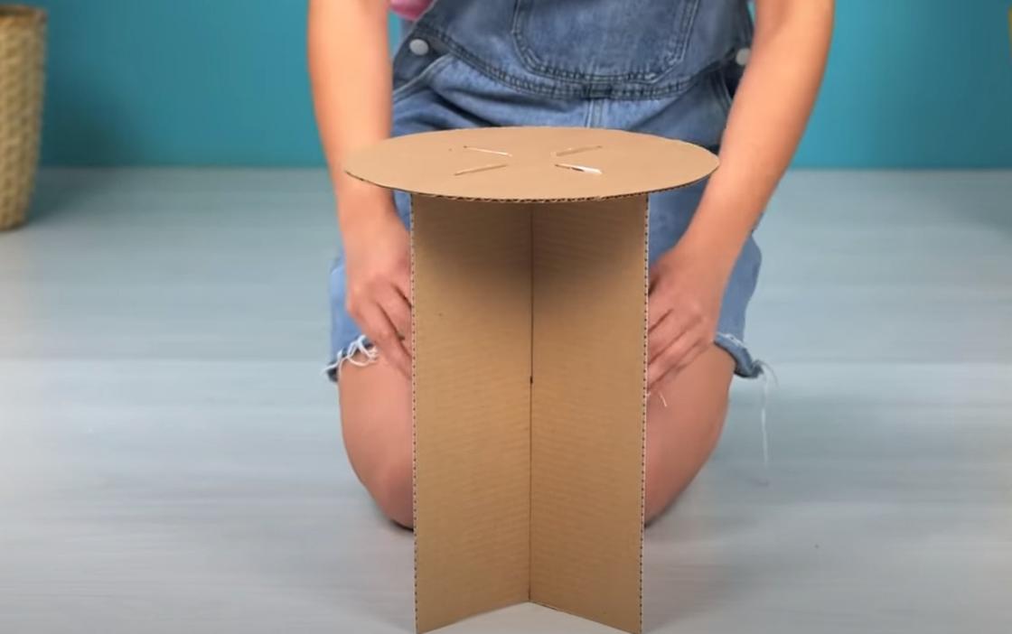 Девушка сидит на полу возле табуретки из картона с круглым сидением