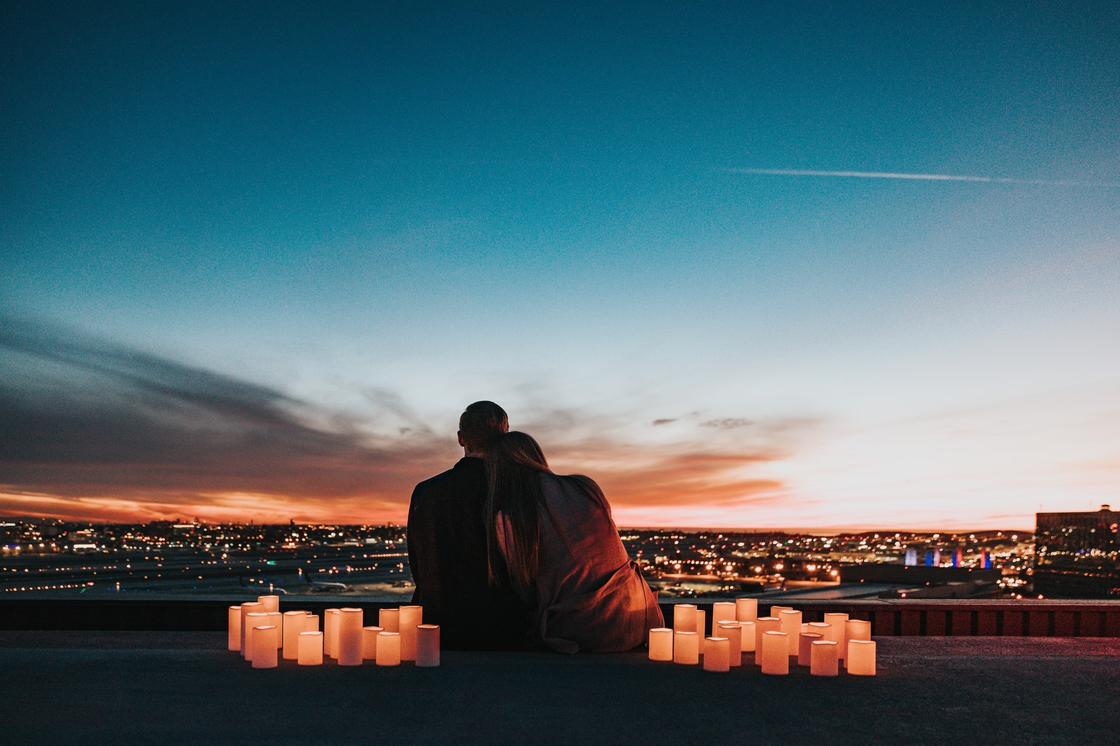 Парень и девушка сидят, обнявшись, на фоне вечерней панорамы города