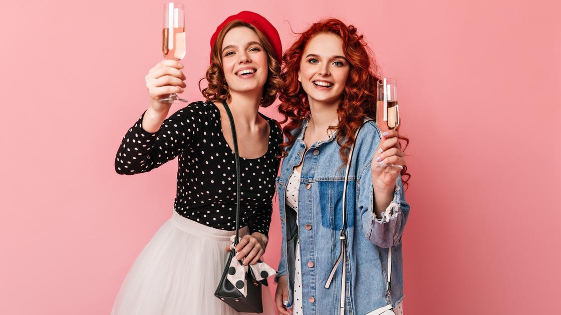 Две девушки держат в руках бокалы с шампанским и улыбаются