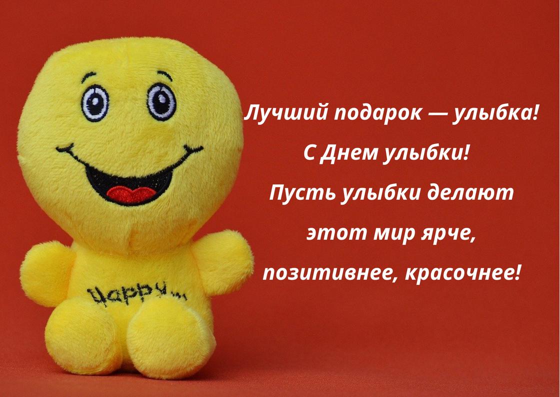 Мягкая игрушка-смайлик с надписью «Happy» улыбается. На открытке с красным фоном написано поздравление с Днем улыбки в прозе