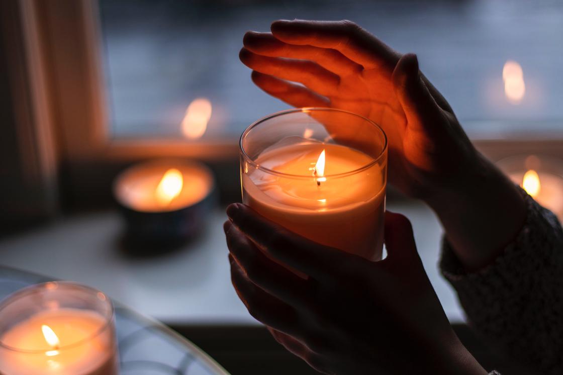Женщина держит в руках зажженую свечу