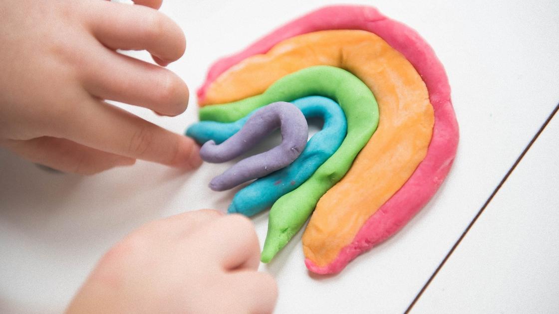 Руки малыша выкладывают кусочки разноцветного пластилина в виде радуги. Используют красный, оранжевый, зеленый, синий и фиолетовый пластилин