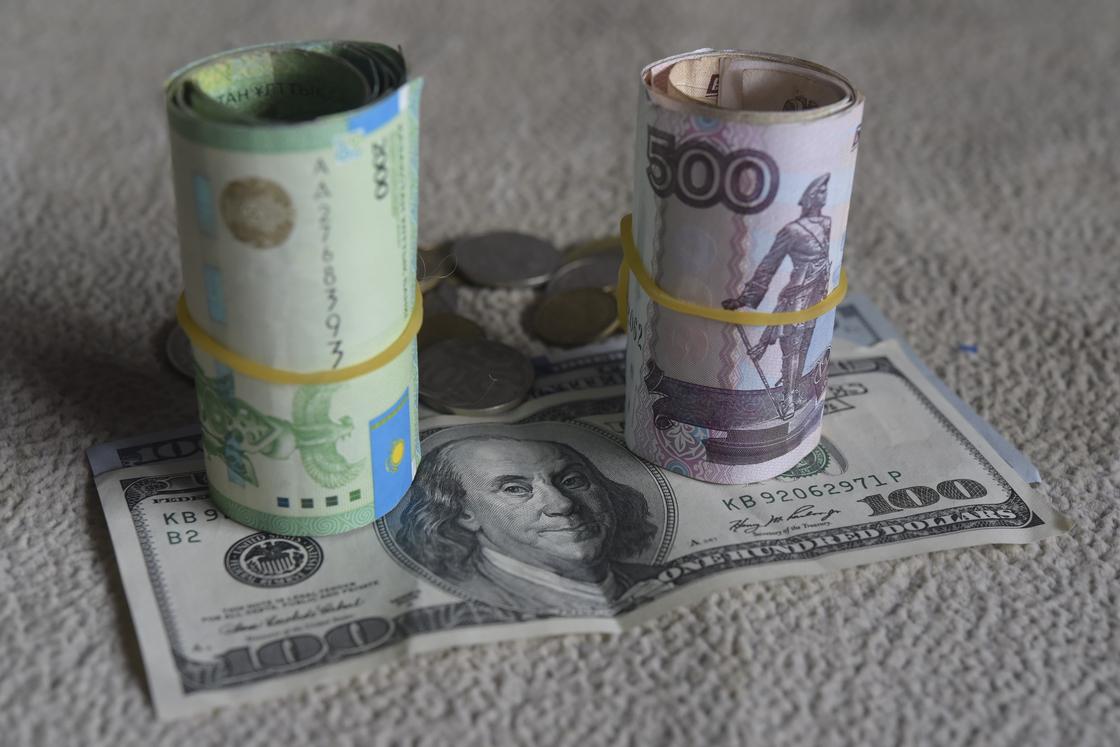 Свернутая пачка тенге стоит рядом со свернутой пачкой рублей на купюре доллара