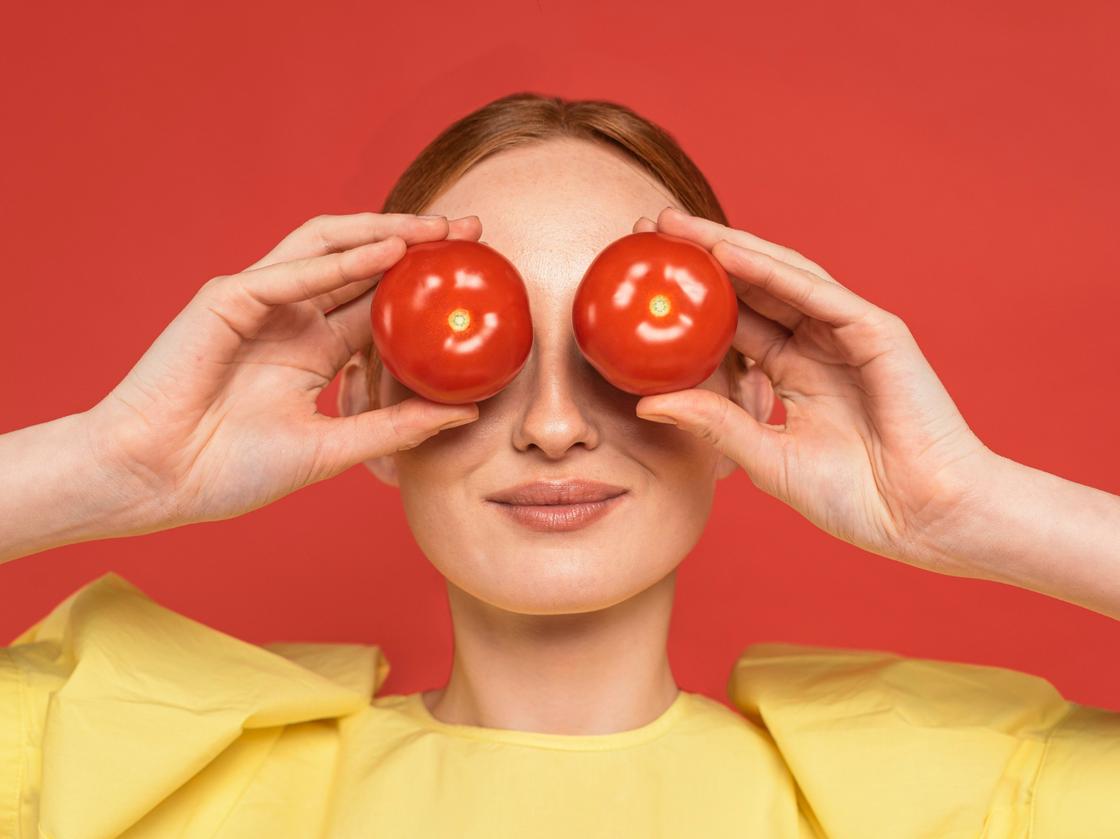 Девушка держит у глаз два помидора