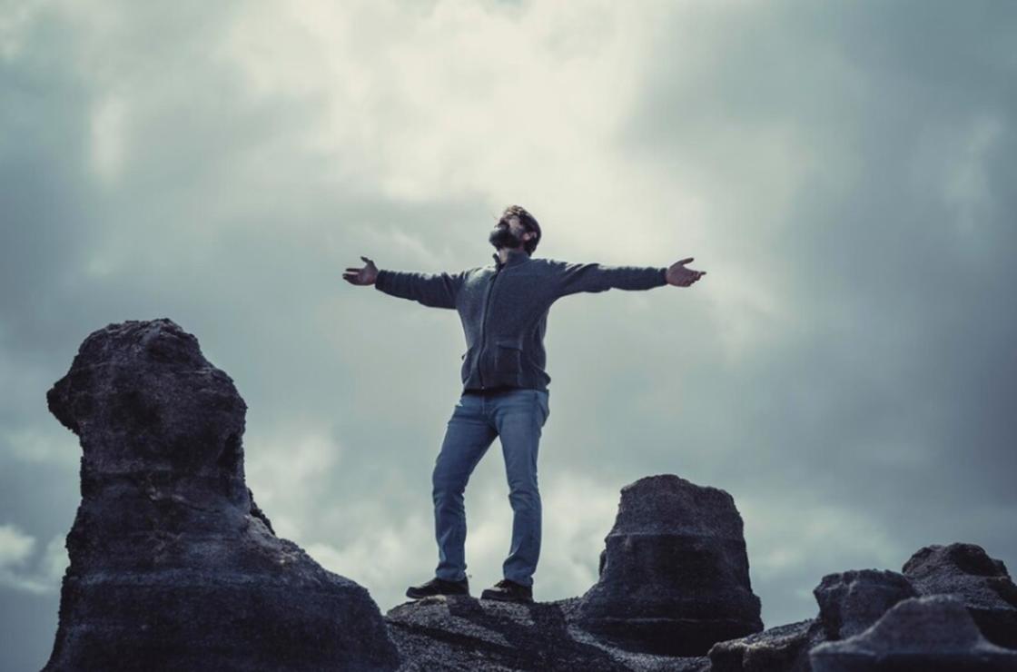 Мужчина стоит на скале с раскинутыми в стороны руками