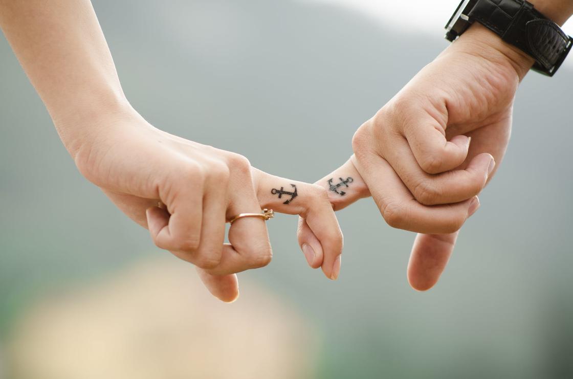 Женская и мужская рука с татуировками в виде якоря на указательных пальцах