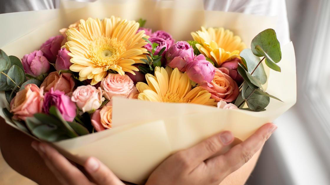 В женских руках объемный букет цветов из эвкалипта, желтых гербер и розовых роз