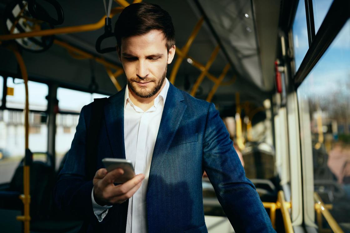 Мужчина в костюме едет в автобусе и смотрит в телефон