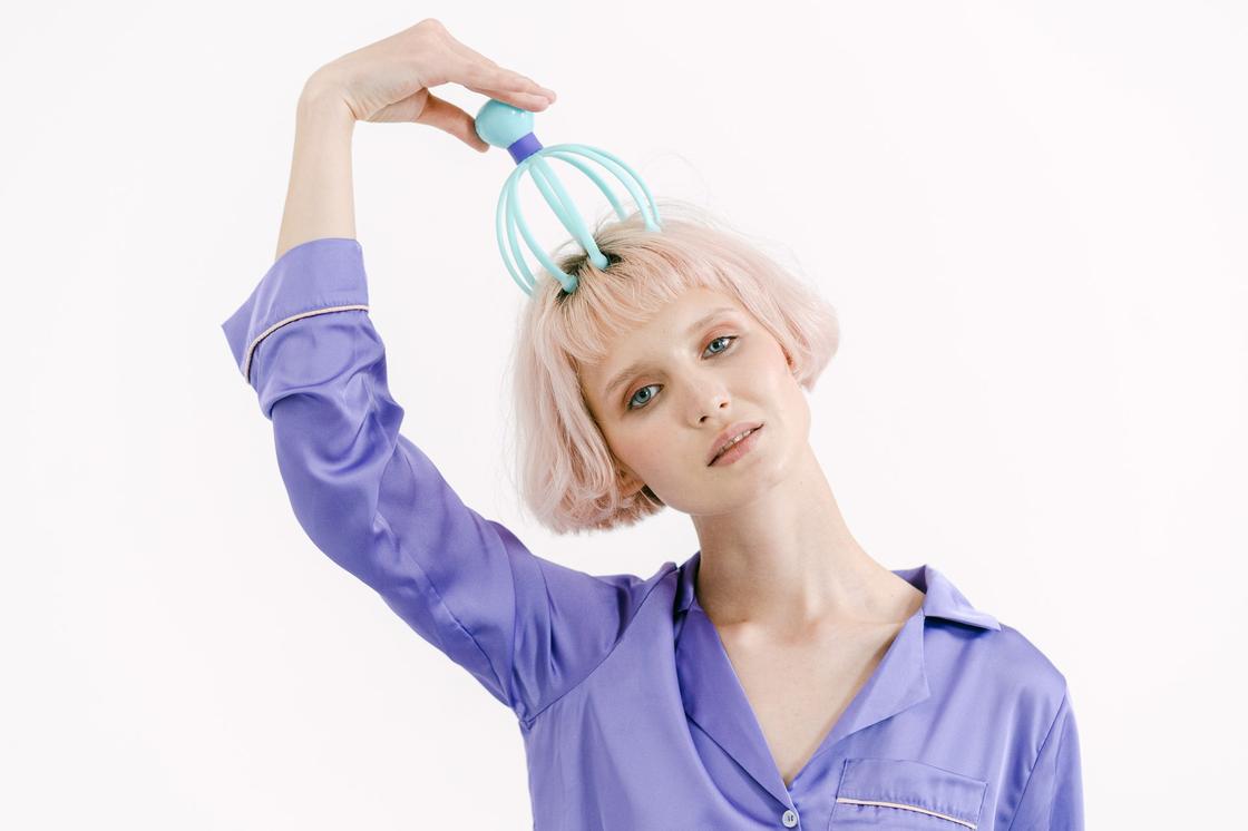 Блондинка в фиолетовой пижаме делает массаж головы на белом фоне