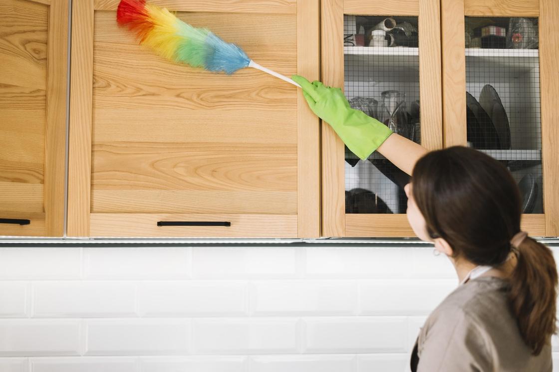 Девушка смахивает пипидастром пыль с подвесного шкафа