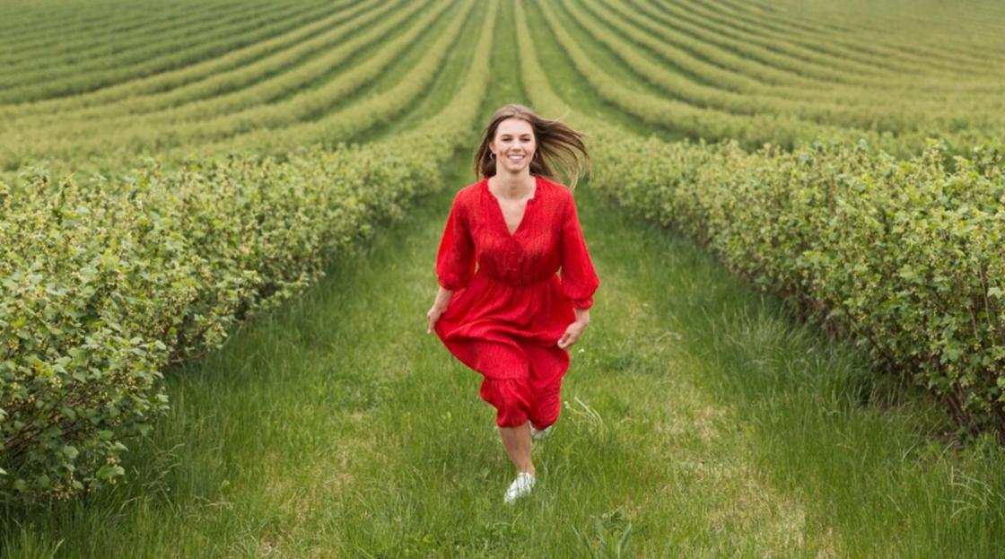 Девушка в красном платье бежит между деревьев