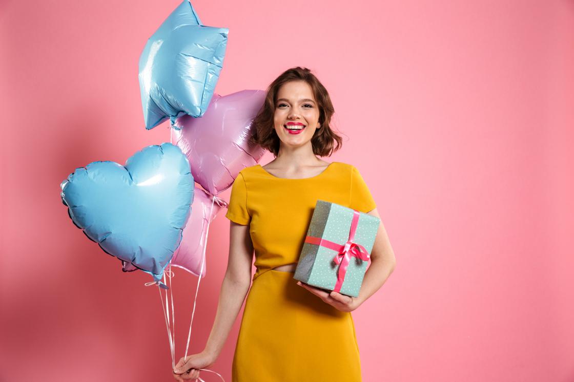 Улыбающаяся девушка держит подарок и воздушные шары