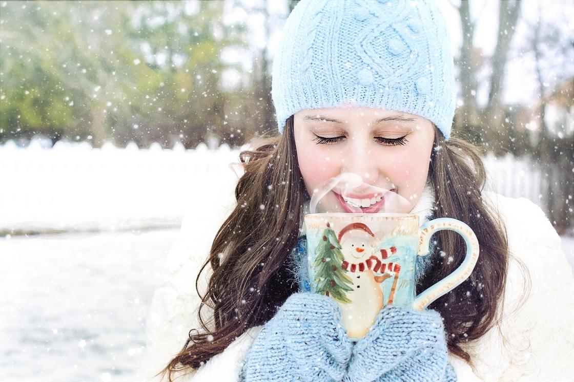 Девушка стоит в зимней одежде на улице с кружкой чая горячего