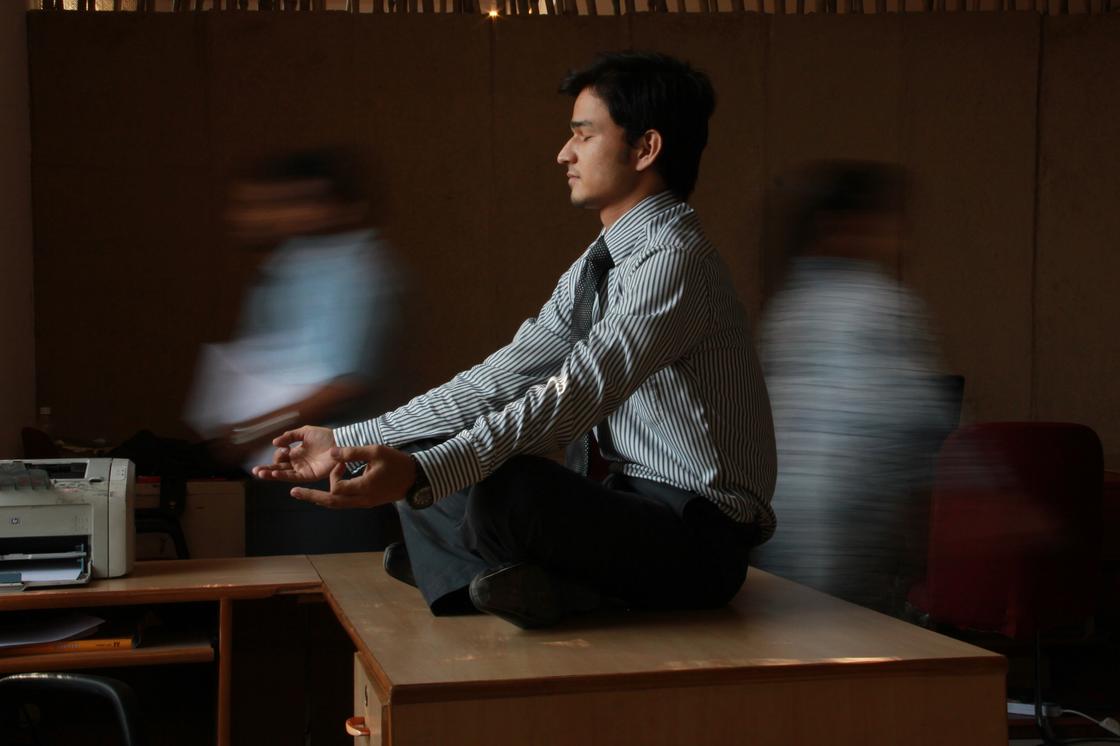 Мужчина в рубашке медитирует сидя на столе