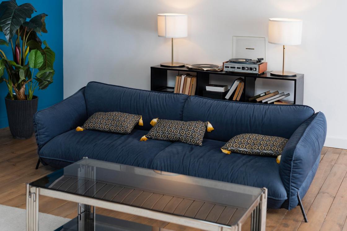 Стильный интерьер с темно-синим диваном, книгами, лампами и прозрачным столом