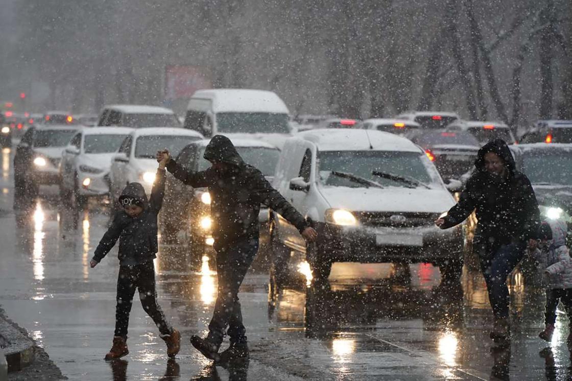 Люди переходят дорогу во время снегопада в Алматы