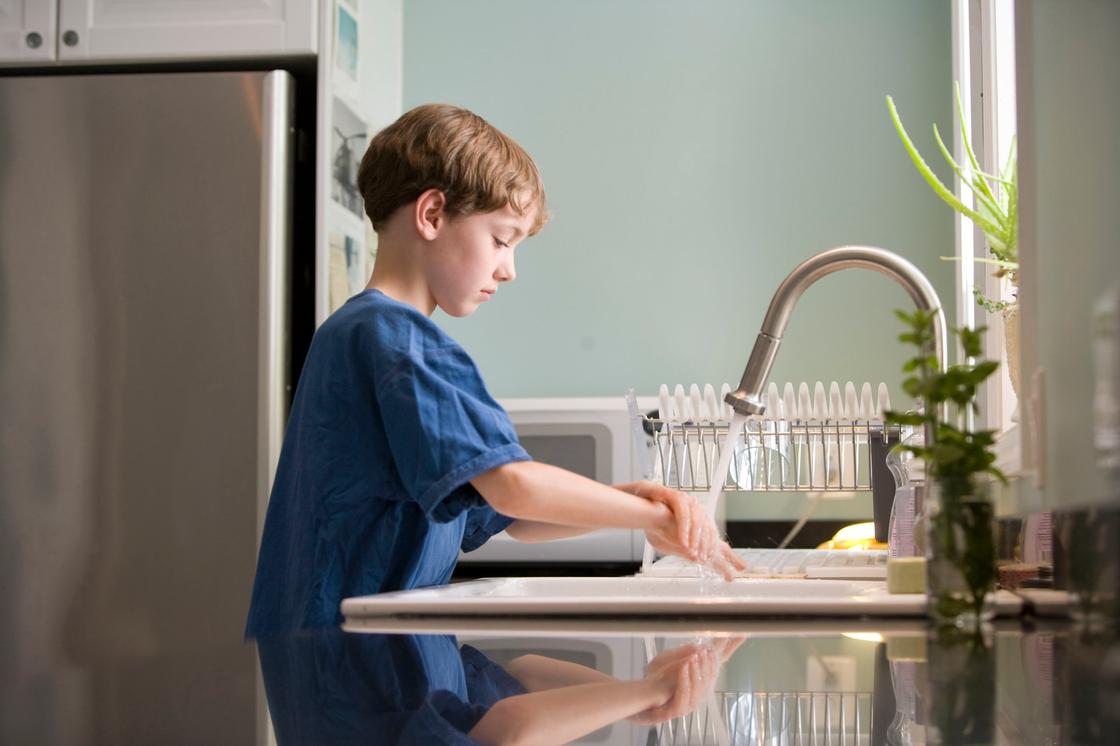 Мальчик моет руки под кухонным краном