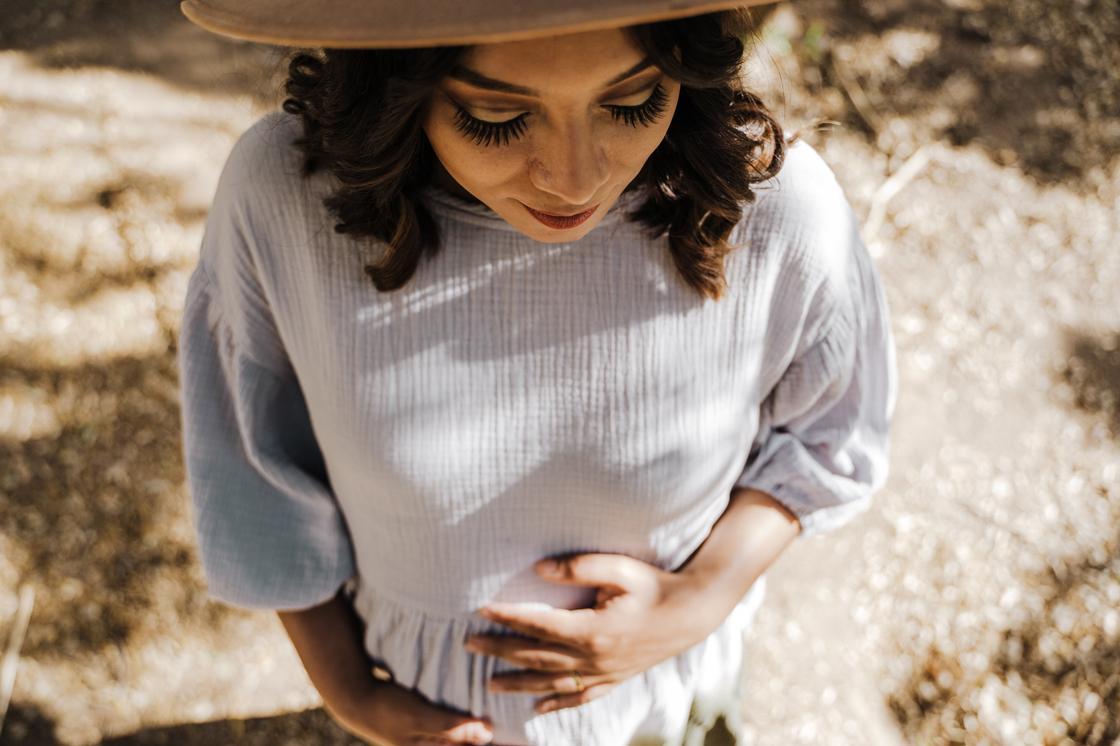 Беременная девушка в шляпе держит свой живот