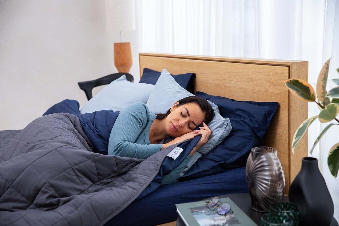 Женщина с голубой футболке спит на кровати. Постельное белье сделано в сине-голубых оттенках