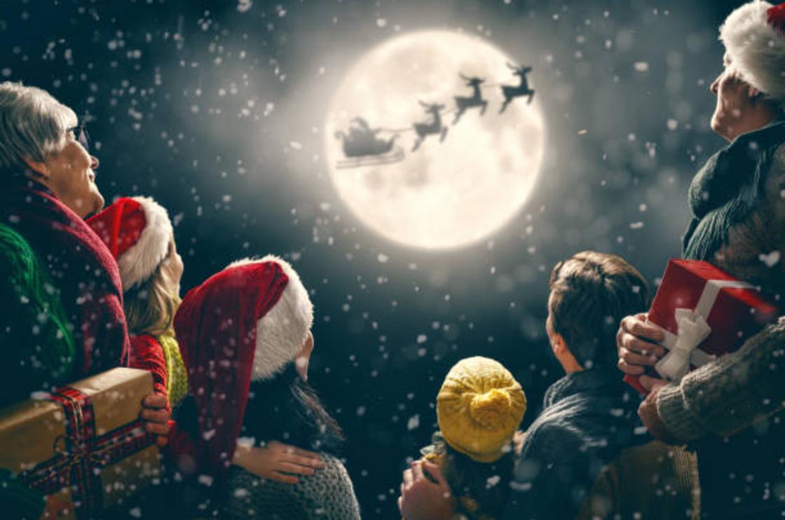 Люди наблюдают за санями Санта-Клауса на фоне Луны