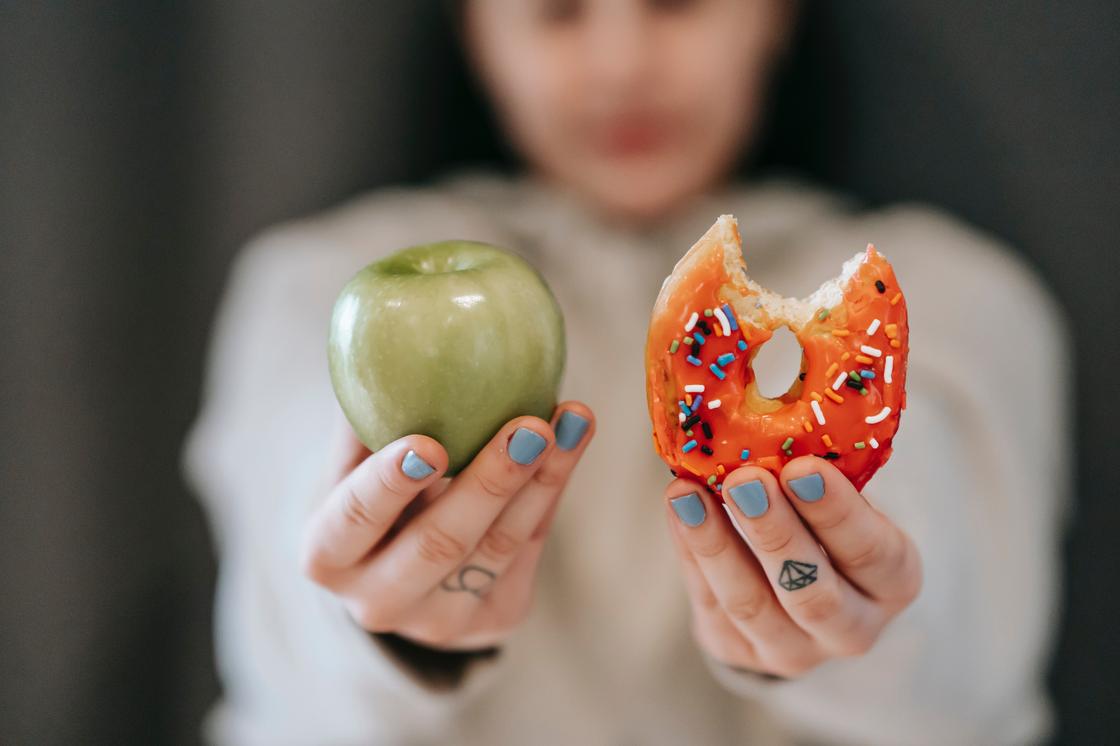 Девушка держит в руке пончик и яблоко